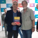 Com o Deputado Federal Gustavo Gayer, de Goiás, que vai falar em um Seminário na ALE/RR. Está levando meu livro sobre a migração venezuelana em Roraima.